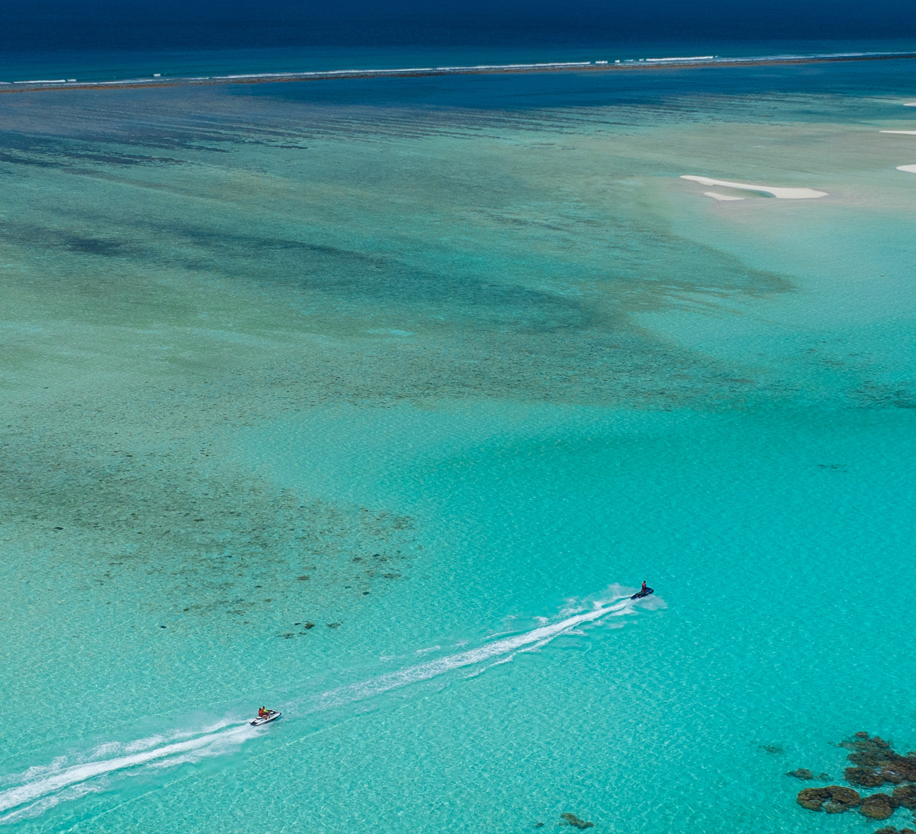 Aerial view of two jet skis riding over a turquoise lagoon where you see a small sandbank formation.